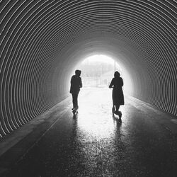 couple riding scooters in tunnel toward light