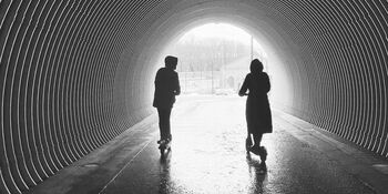 couple riding scooters in tunnel toward light